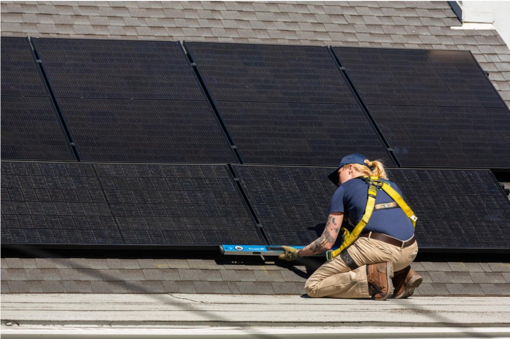 Installer leveling a solar panel on a shingle roof